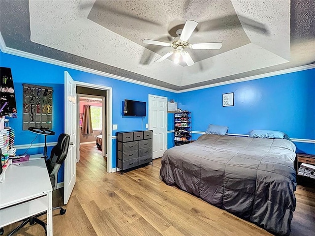 bedroom featuring a ceiling fan, a textured ceiling, wood finished floors, baseboards, and a tray ceiling