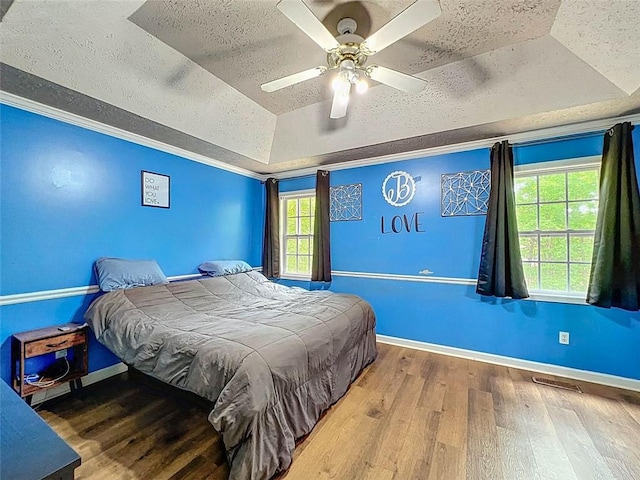 bedroom with baseboards, a tray ceiling, a textured ceiling, and wood finished floors
