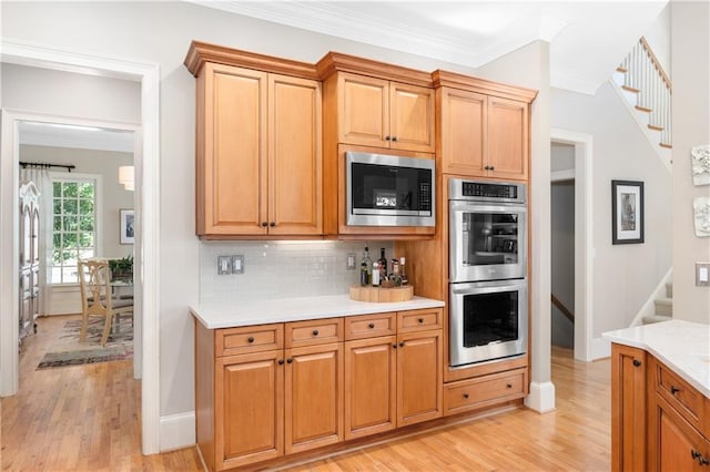 kitchen featuring crown molding, light wood finished floors, light countertops, and appliances with stainless steel finishes