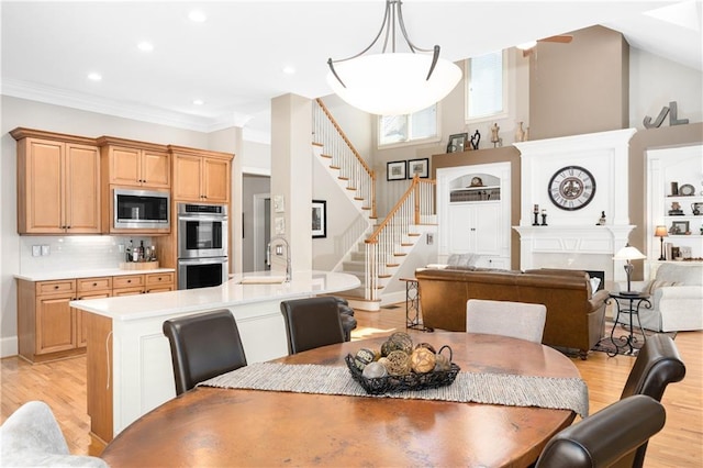 dining space featuring stairs, ornamental molding, light wood-style flooring, a fireplace, and a high ceiling