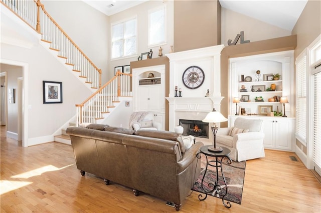 living room with a wealth of natural light, built in features, stairs, and light wood-type flooring