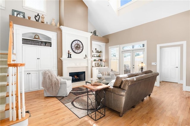 living room featuring stairway, built in features, light wood finished floors, high vaulted ceiling, and a large fireplace