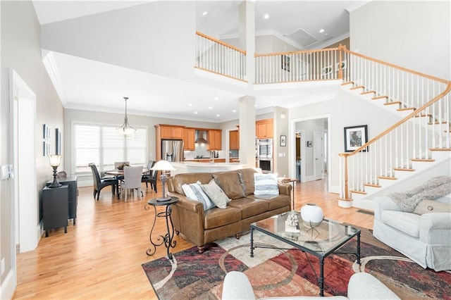 living area with high vaulted ceiling, stairway, crown molding, light wood finished floors, and baseboards