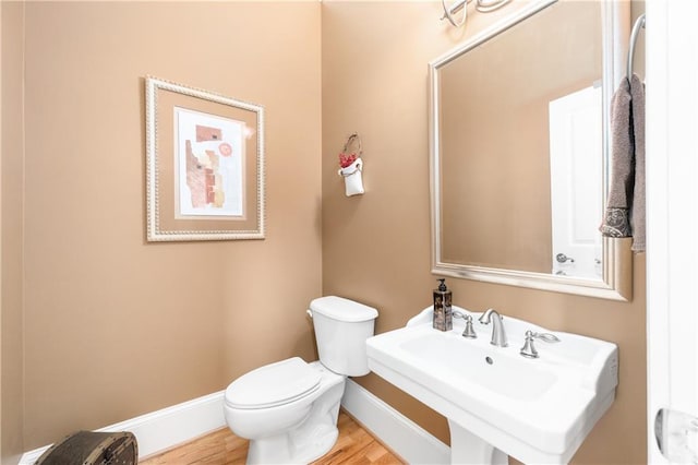 half bathroom with a sink, baseboards, toilet, and wood finished floors