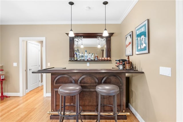 bar featuring wood finished floors, a bar, crown molding, baseboards, and hanging light fixtures