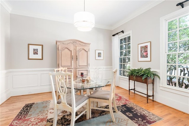 dining space featuring light wood finished floors, a wainscoted wall, a decorative wall, and crown molding