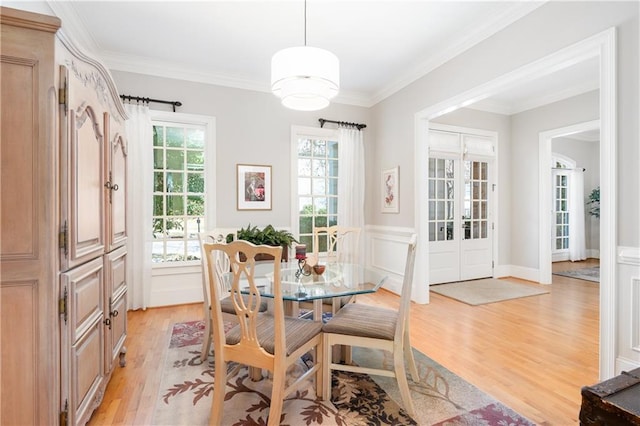 dining room featuring a wainscoted wall, french doors, crown molding, a decorative wall, and light wood-type flooring