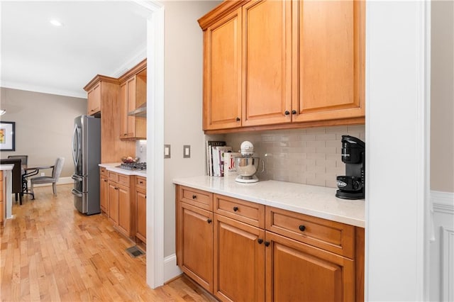 kitchen featuring visible vents, light wood finished floors, freestanding refrigerator, ornamental molding, and backsplash