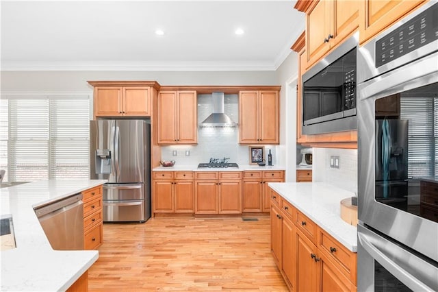 kitchen with light wood-type flooring, ornamental molding, stainless steel appliances, wall chimney exhaust hood, and tasteful backsplash