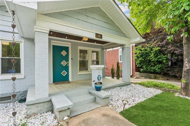 view of exterior entry with brick siding and covered porch