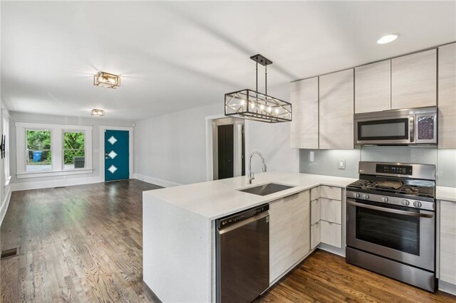 kitchen featuring stainless steel appliances, a sink, open floor plan, a peninsula, and light countertops
