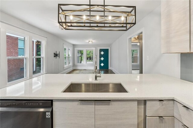 kitchen with a notable chandelier, light stone countertops, stainless steel dishwasher, a sink, and open floor plan