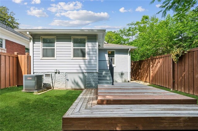 rear view of house with central AC unit, a wooden deck, a fenced backyard, and a lawn