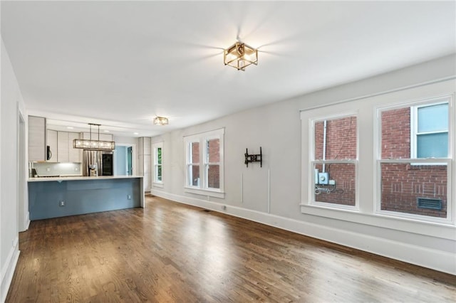 unfurnished living room featuring an inviting chandelier, dark wood-style flooring, and baseboards