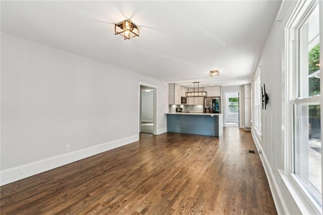 unfurnished living room with an inviting chandelier, visible vents, baseboards, and dark wood-style floors