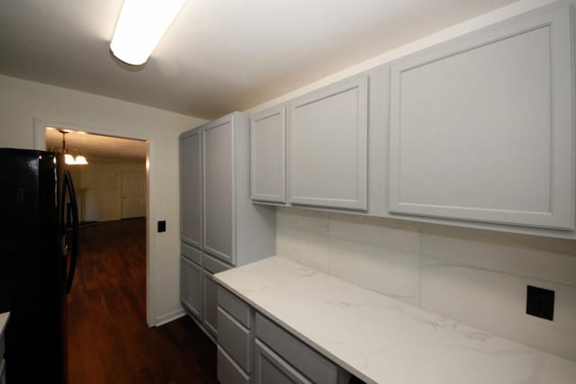 kitchen featuring an inviting chandelier, black fridge, dark wood-type flooring, and light stone counters