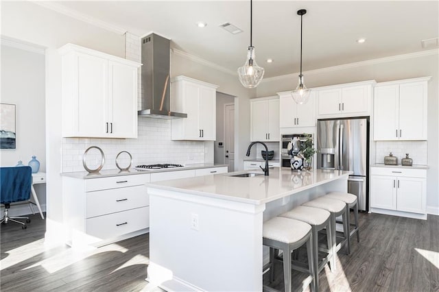 kitchen with sink, appliances with stainless steel finishes, white cabinetry, a center island with sink, and wall chimney exhaust hood