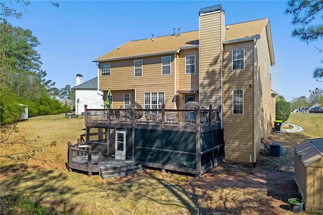 rear view of property featuring a lawn, a chimney, central AC, and a deck