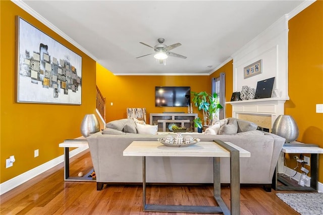 living area with a fireplace, wood finished floors, ceiling fan, and ornamental molding