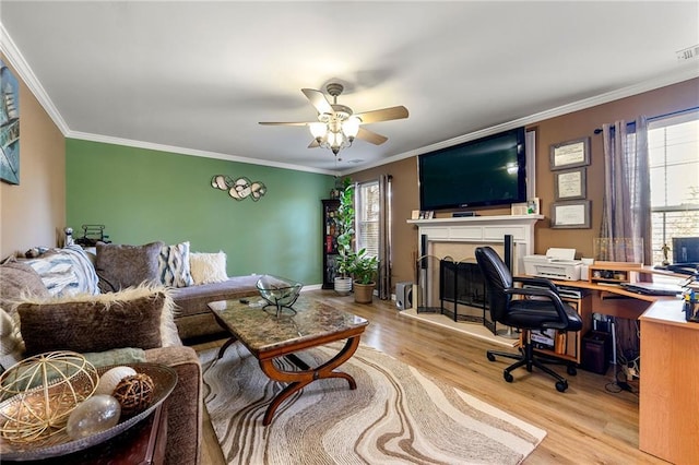 living area featuring ceiling fan, wood finished floors, crown molding, and a fireplace with raised hearth