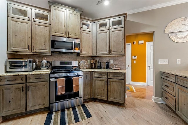kitchen featuring a toaster, crown molding, tasteful backsplash, appliances with stainless steel finishes, and light wood-type flooring