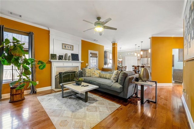 living area with ceiling fan, a large fireplace, crown molding, and hardwood / wood-style flooring