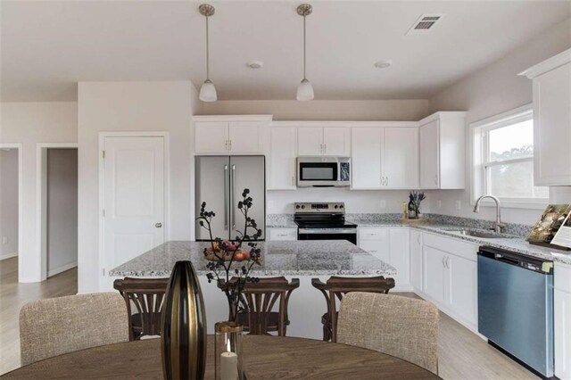 kitchen featuring white cabinets, a kitchen island, hanging light fixtures, and appliances with stainless steel finishes