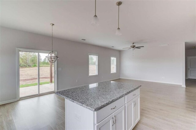 kitchen with light stone countertops, ceiling fan, pendant lighting, white cabinets, and light wood-type flooring