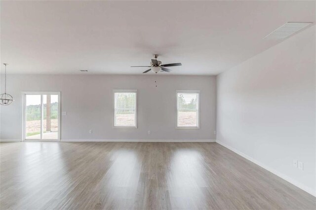 empty room featuring ceiling fan with notable chandelier and light hardwood / wood-style floors