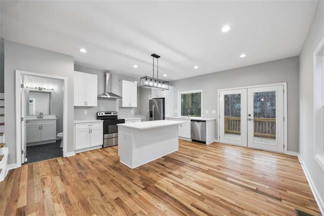 kitchen with white cabinets, appliances with stainless steel finishes, a center island, light countertops, and wall chimney range hood