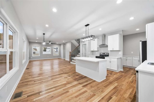 kitchen with light countertops, visible vents, wall chimney range hood, stainless steel electric range, and fridge