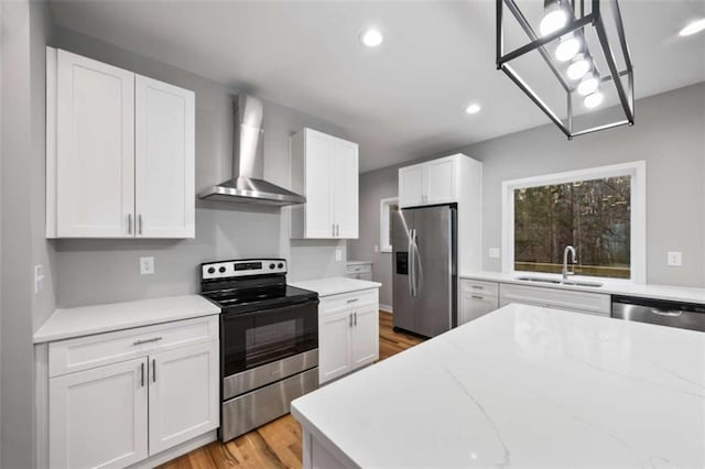 kitchen featuring stainless steel appliances, light wood-style floors, white cabinetry, a sink, and wall chimney range hood