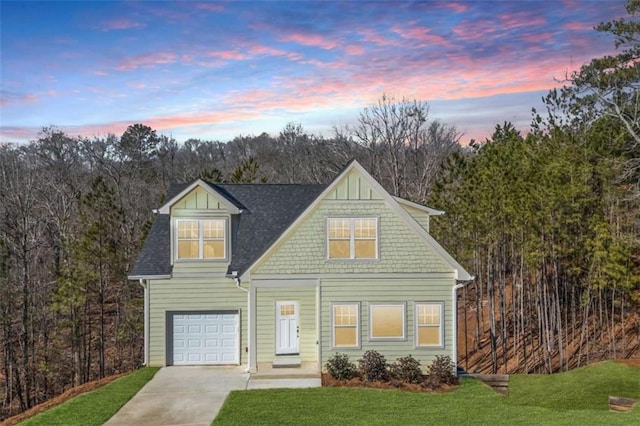 view of front of house featuring driveway, a shingled roof, a view of trees, and a lawn