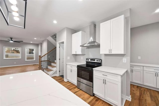 kitchen featuring electric stove, recessed lighting, light wood-style flooring, white cabinets, and wall chimney range hood