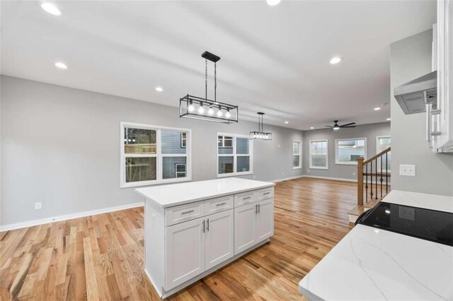 kitchen with white cabinetry, a kitchen island, hanging light fixtures, and light wood finished floors