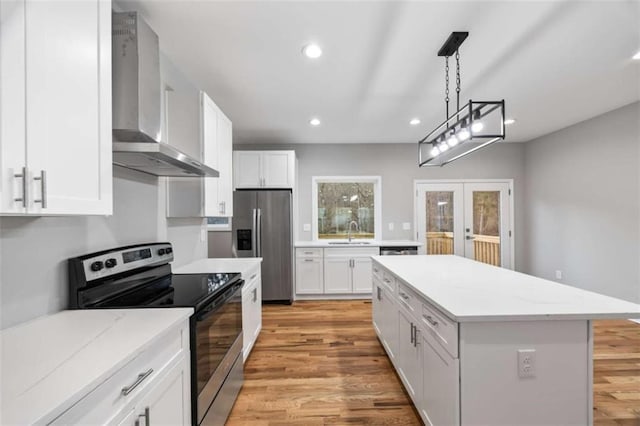 kitchen with stainless steel appliances, a sink, white cabinets, french doors, and wall chimney exhaust hood