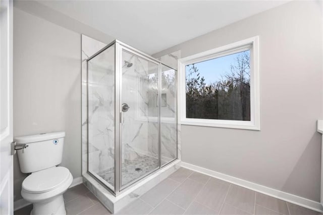 bathroom featuring toilet, a marble finish shower, baseboards, and tile patterned floors