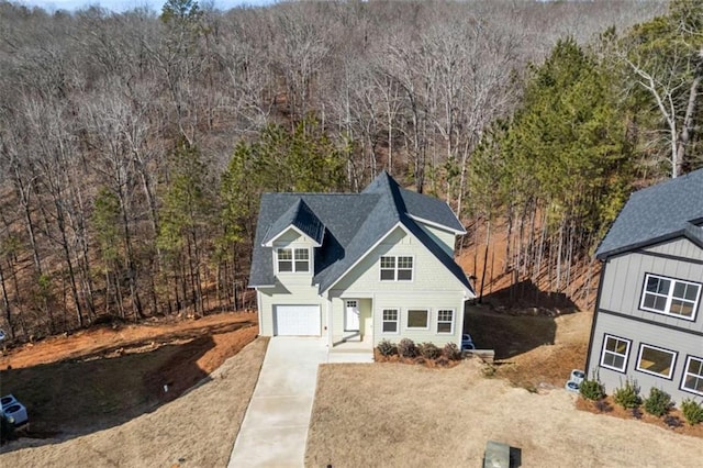 view of front facade with a garage, concrete driveway, and a wooded view