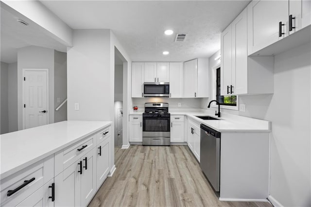 kitchen featuring visible vents, white cabinets, a sink, light wood finished floors, and stainless steel appliances