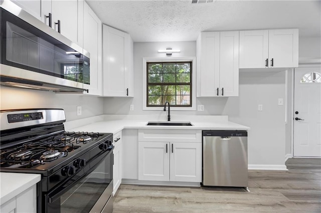 kitchen with stainless steel appliances, white cabinetry, a sink, and light wood-type flooring