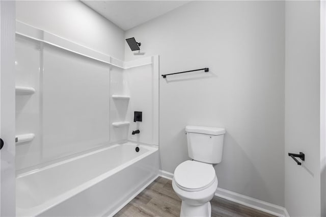 bathroom featuring toilet, baseboards,  shower combination, and wood finished floors