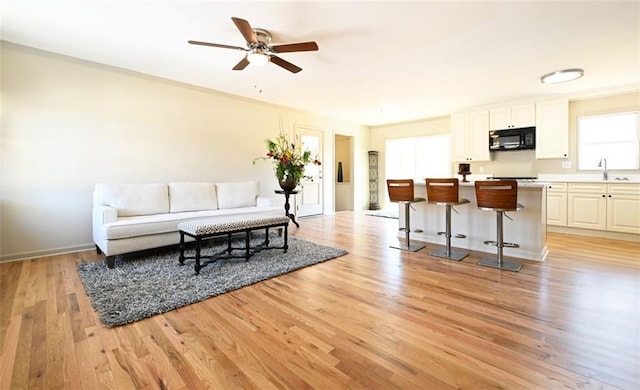 living room featuring baseboards, a ceiling fan, and light wood-style floors