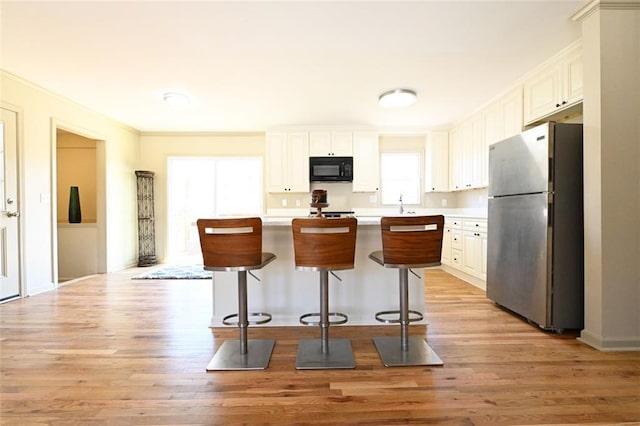 kitchen with light wood finished floors, a breakfast bar, freestanding refrigerator, black microwave, and light countertops