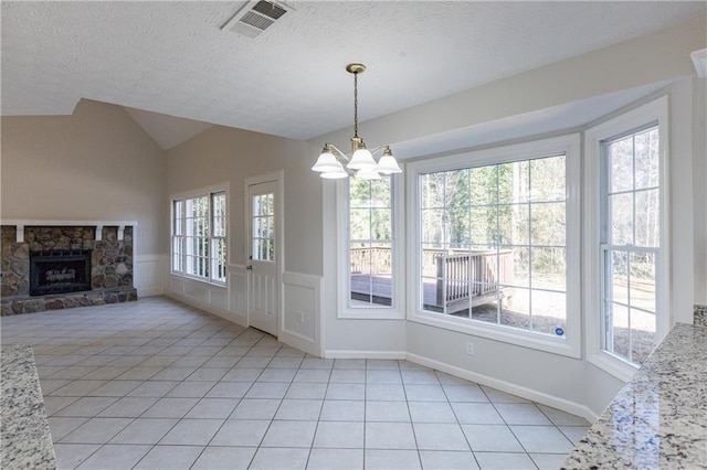 unfurnished dining area with light tile patterned flooring, vaulted ceiling, a stone fireplace, and a textured ceiling