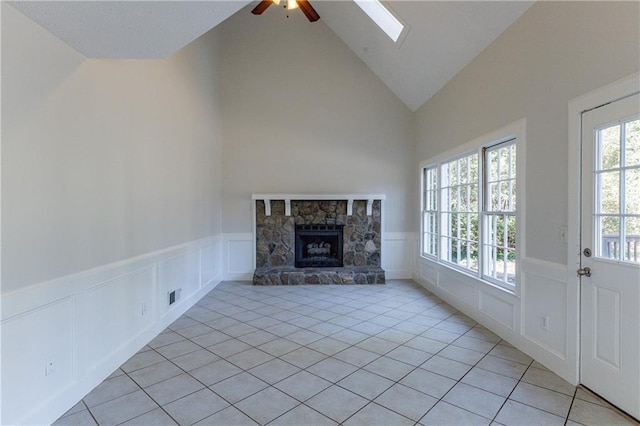 unfurnished living room with light tile patterned floors, a stone fireplace, vaulted ceiling with skylight, and ceiling fan