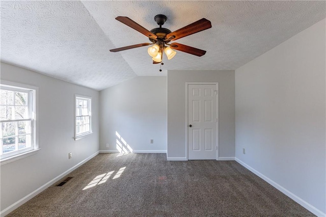 unfurnished room featuring vaulted ceiling, ceiling fan, dark carpet, and a textured ceiling