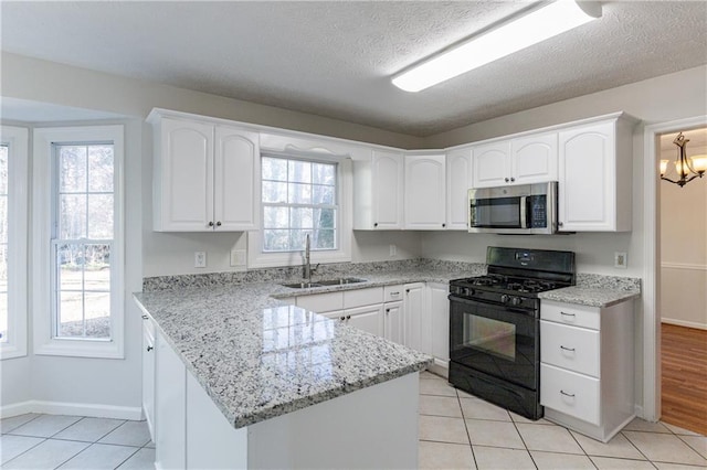 kitchen with sink, white cabinetry, light stone counters, a chandelier, and black gas range