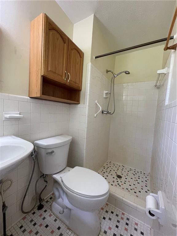 bathroom featuring tiled shower, toilet, tile patterned floors, and tile walls