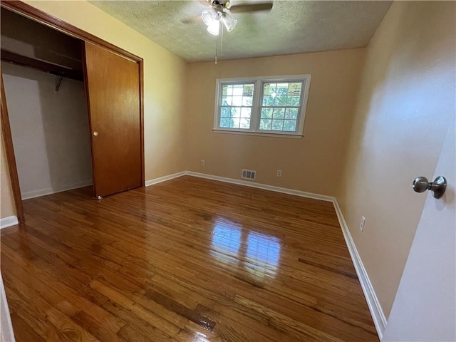 unfurnished bedroom featuring ceiling fan, a closet, a textured ceiling, and dark hardwood / wood-style floors