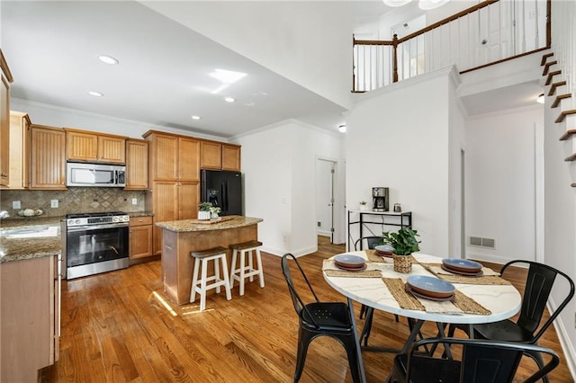 224 Celestial Ridge Dr, Dallas, GA 30132 - kitchen with stainless steel appliances, a kitchen island, light wood-style flooring, tasteful backsplash, and ornamental molding